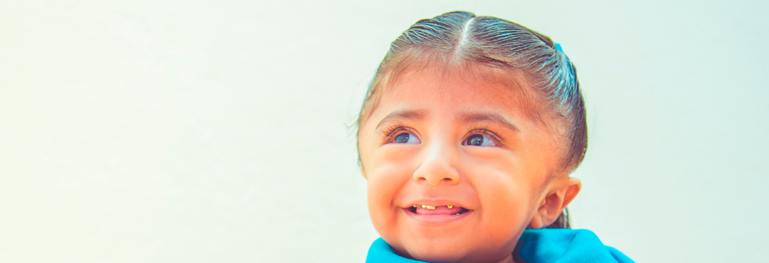 Niña con blusa azul sonríe mirando al horizonte
