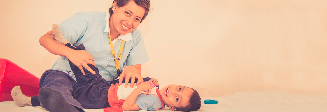 Imagen de niño con su terapeuta físico. La terapeuta está realizando estiramientos en la pierna del niño.