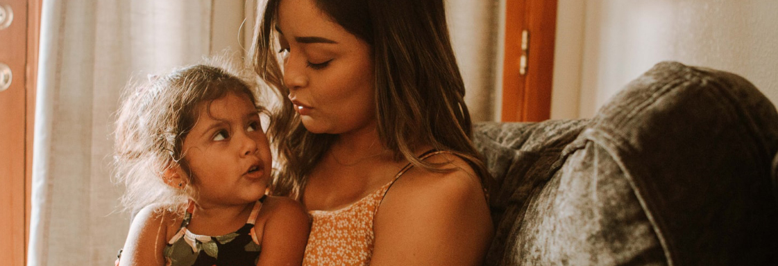 Fotografía de madre e hija. La niña tiene alrededor de 5 años. Está sentada en las piernas de su madre. Ambas están platicando.